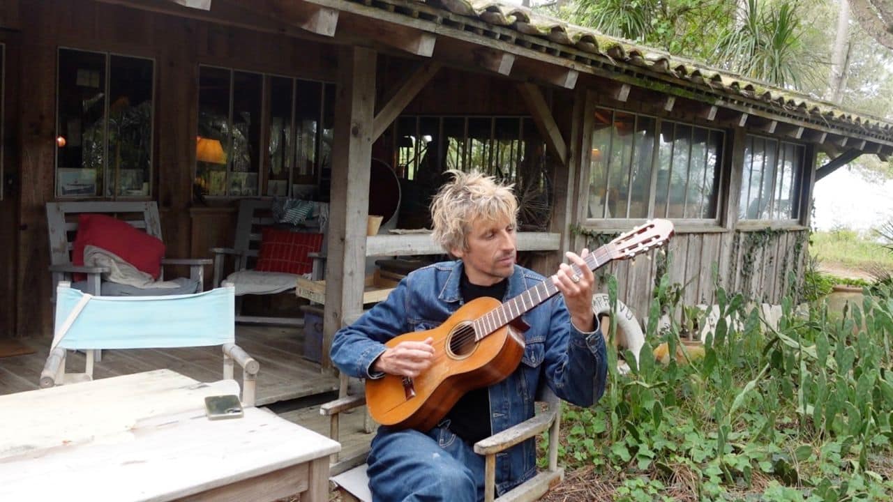Antonin Bartherotte jouant de la guitare devant sa cabane à la Pointe du Cap Ferret